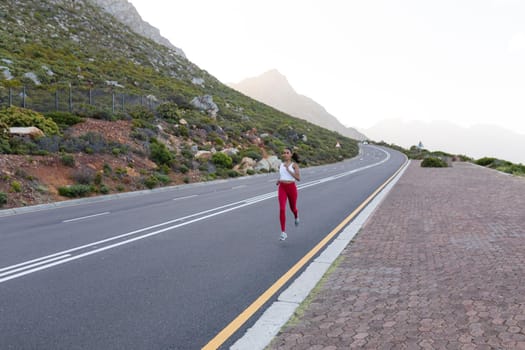 Fit african american woman in sportswear running on a coastal road. looking at the camera and smiling. healthy lifestyle, exercising in nature.
