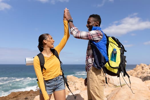 Fit afrcan american couple wearing backpacks high fiving hiking on the coast. healthy lifestyle, exercising in nature.