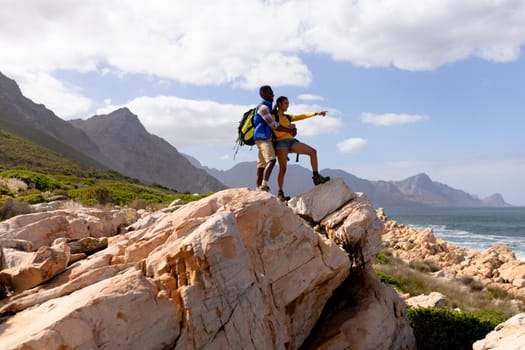 Fit afrcan american couple wearing backpacks hiking embracing on the coast. healthy lifestyle, exercising in nature.