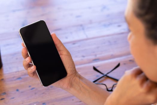 Caucasian woman using smartphone sitting by table at home. Staying at home in self isolation during quarantine lockdown.