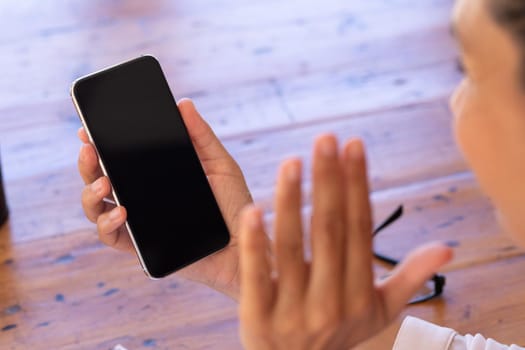 Caucasian woman using smartphone on video call at home, waving. Staying at home in self isolation during quarantine lockdown.