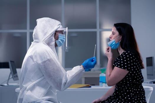 Caucasian male medical worker wearing protective clothing taking dna swab of masked patient. healthcare, medical research technology and hygiene during coronavirus covid 19 pandemic.
