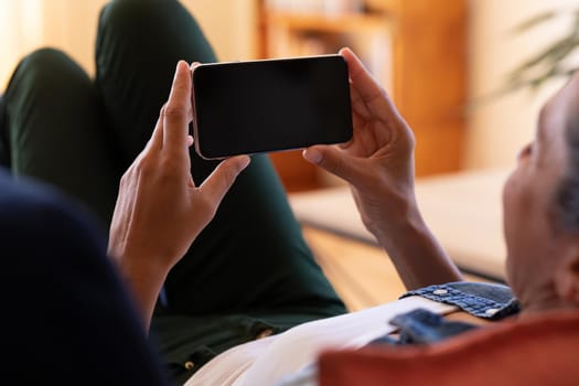 Caucasian woman using smartphone lying on sofa at home. Staying at home in self isolation during quarantine lockdown.