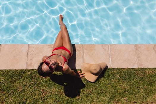 Mixed race woman sunbathing by pool on a sunny day. Hanging out and relaxing outdoors in summer.