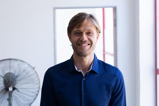 Portrait of smiling caucasian man standing in front of window in white room. self isolating at home durimg quaratine lockdown.
