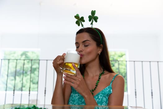 Caucasian woman celebrating st patrick's day making video call wearing deely boppers drinking beer. staying at home in isolation during quarantine lockdown.