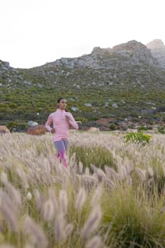 Fit african american woman in sportswear running through tall grass. healthy lifestyle, exercising in nature.