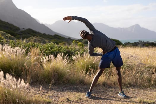 Fit african american man in sportswear stretching in tall grass. healthy lifestyle, exercising in nature.