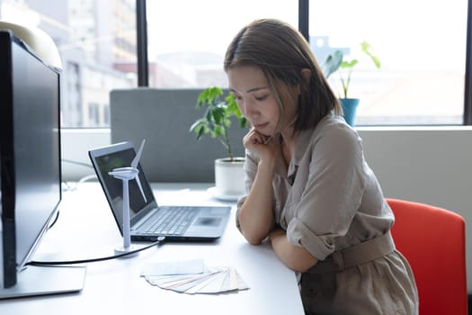 Asian businesswoman wearing face mask sitting at desk looking at samples in creative office. social distancing protection hygiene in workplace during covid 19 pandemic.