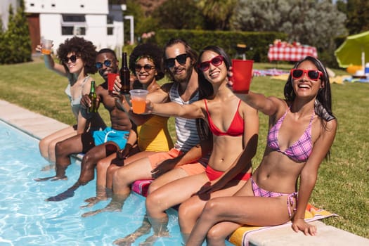 Diverse group of friends drinking beer and sitting at the poolside. Hanging out and relaxing outdoors in summer.