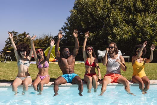 Diverse group of friends smiling and sitting at the poolside. Hanging out and relaxing outdoors in summer.