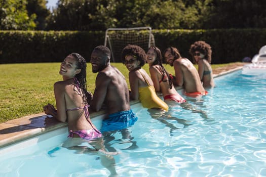 Diverse group of friends smiling and leaning on the poolside. Hanging out and relaxing outdoors in summer.