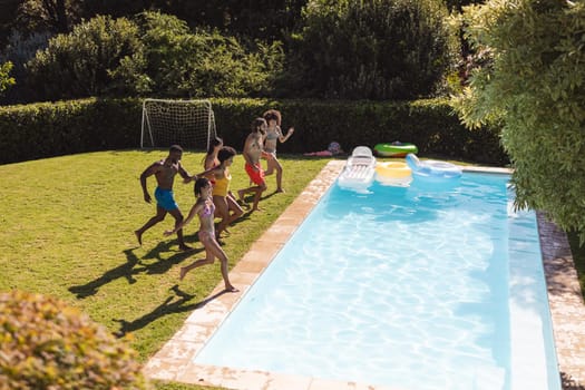 Diverse group of friends having fun and jumping into water at a pool party. Hanging out and relaxing outdoors in summer.