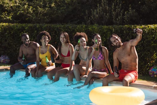 Diverse group of friends drinking beer and taking selfie at the poolside. Hanging out and relaxing outdoors in summer.