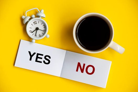 Yes and no text on notepad with alarm clock and coffee cup on yellow background. Decision and business concept.