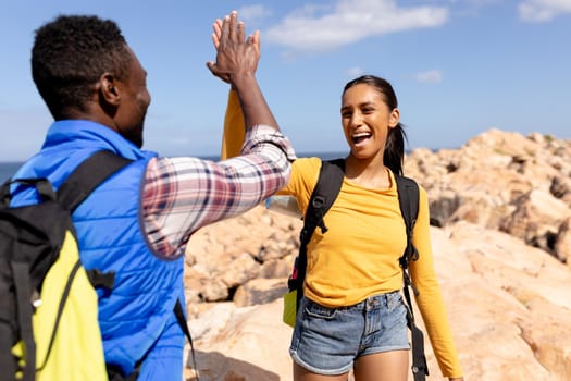 Fit afrcan american couple wearing backpacks high fiving hiking on the coast. healthy lifestyle, exercising in nature.