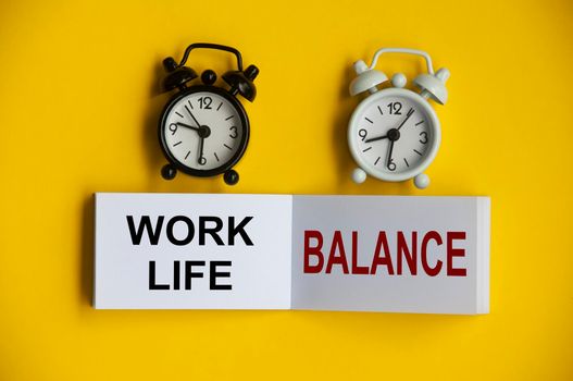 work life balance text on notepad with alarm clocks on yellow background.