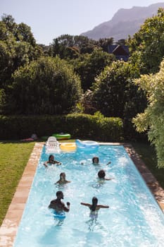 Diverse group of friends having fun in swimming pool. Hanging out and relaxing outdoors in summer.