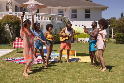 Diverse group of friends dancing and smiling at a pool party. Hanging out and relaxing outdoors in summer.