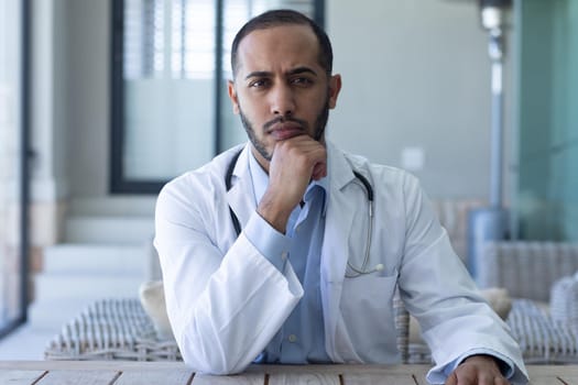 Portrait of caucasian male doctor looking at the camera and rubbing his chin. professional medical worker wearing stethoscope and lab coat.