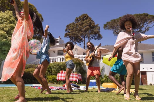 Diverse group of friends dancing and smiling at a pool party. Hanging out and relaxing outdoors in summer.