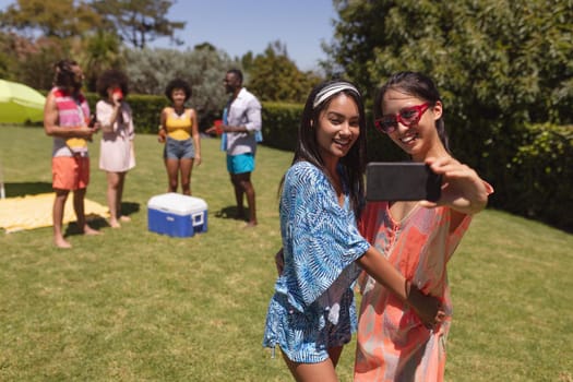 Two mixed race female friends taking selfie at a pool party. Hanging out and relaxing outdoors in summer.