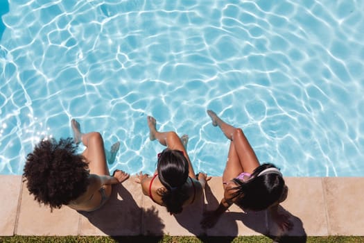 Diverse group of female friends sitting at the poolside. hanging out and relaxing outdoors in summer.