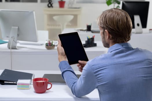 Rear view of caucasian businessman sitting at desk making video call using tabet. working online, social distancing during quarantine lockdown.