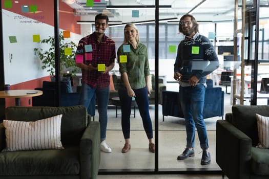 Diverse group of business people working in creative office. group of people brainstorming and taking notes on glass board. business people and work colleagues at a busy creative office.