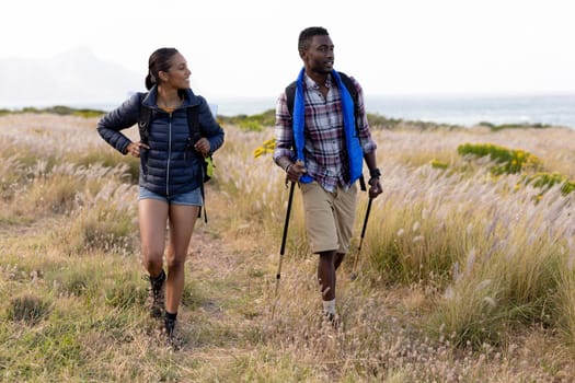 Fit african american couple wearing backpacks hiking in coastal countryside. healthy lifestyle, exercising in nature.