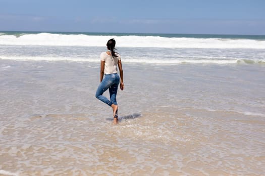 African american woman walking on a beach by the sea. healthy lifestyle, leisure in nature.