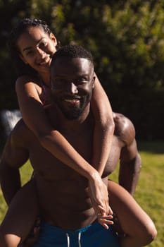 Portrait of two diverse male and female friends man carrying on back and smiling. Hanging out and relaxing outdoors in summer.