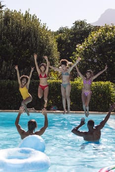 Diverse group of female friends jumping into water at a pool party. Hanging out and relaxing outdoors in summer.