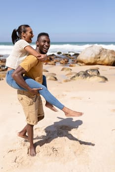 African american couple piggybacking on a beach by the sea. healthy lifestyle, leisure in nature.