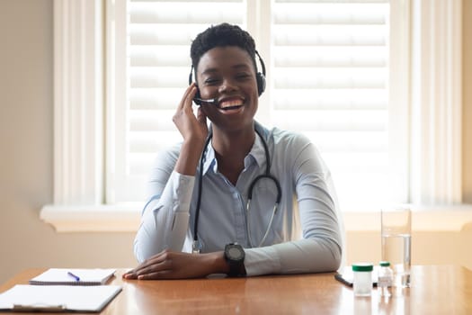 African american doctor wearing phone headset talking while having a videocall at home. distant communication and telemedicine consultation concept.