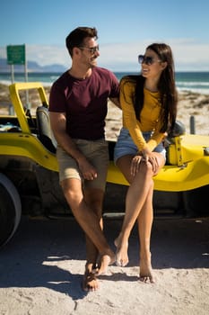 Happy caucasian couple sitting on beach buggy by the sea embracing. beach break on summer holiday road trip.