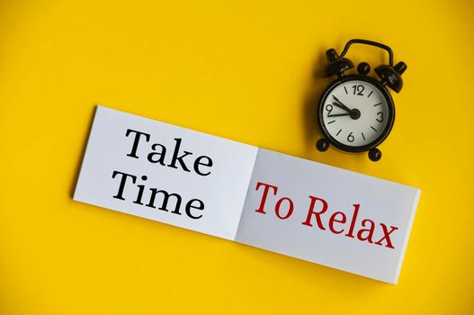 Take time to relax text on notepad with alarm clock on yellow background. Lifestyle concept