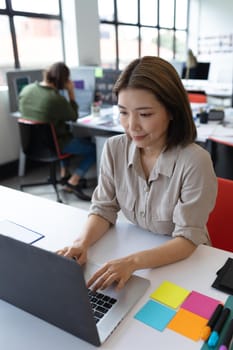 Asian businesswoman working in creative office. woman sitting at desk and using laptop computer. social distancing in workplace during covid 19 pandemic.