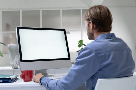 Rear view of caucasian businessman sitting at desk making video call using desktop computer. working online, social distancing during quarantine lockdown.