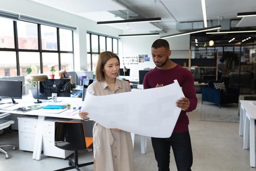 Diverse male and female colleague looking at blueprints and discussing. business people and work colleagues at a busy creative office.