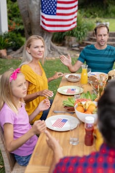 Caucasian man saying grace with family before eating meal together in garden. three generation family celebrating independence day eating outdoors together.