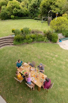 High angle view of caucasian three generation family sitting at table eating meal in garden. three generation family celebrating eating outdoors together.