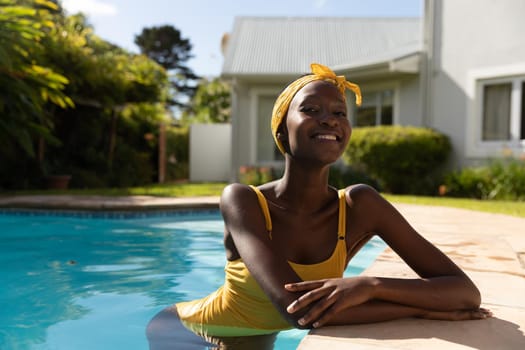 Portrait of african american woman in water leaning on poolside on sunny garden terrace. staying at home in isolation during quarantine lockdown.