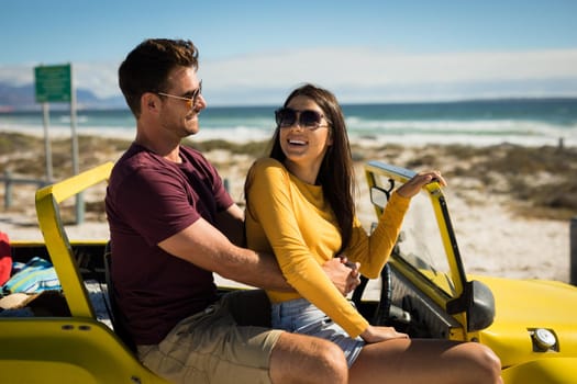 Happy caucasian couple sitting on beach buggy by the sea embracing. beach break on summer holiday road trip.