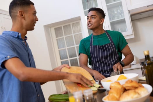 Diverse gay male couple spending time in kitchen cooking together and talking. staying at home in isolation during quarantine lockdown.