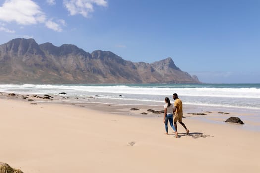 African american couple walking holding hands on a beach by the sea. healthy lifestyle, leisure in nature.