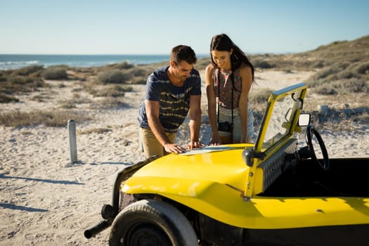 Happy caucasian couple reading roadmap on beach buggy by the sea. beach break on summer holiday road trip.