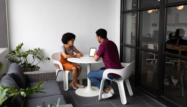 Two mixed race business people working in creative office. two people sitting and discussing work. business people and work colleagues at a busy creative office.