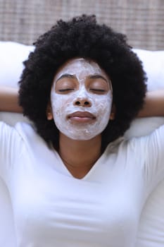 African american woman lying in bed wearing beauty mask. staying at home in isolation during quarantine lockdown.