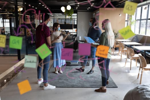 Diverse group of business people working in creative office. group of people wearing face masks and discussing work. social distancing protection hygiene in workplace during covid 19 pandemic.